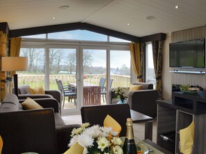 Een ruime woonkamer met een grote schuifpui naar een terras, een flatscreen televisie aan de muur en een tafel met champagne en bloemen.