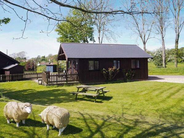 A rustic wooden building with a picnic table and a fenced area.