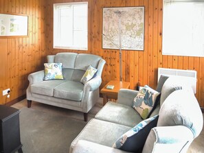 A room with a wooden paneled wall, a grey sofa, a small table, and a radiator. - 2 bedroom accommodation in Nawton, near Helmsley (Nawton, near Helmsley)