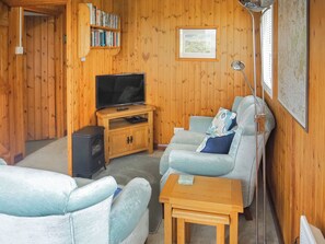 Una habitación con paneles de madera, un televisor, una estantería, un cuadro enmarcado y una ventana con persianas.