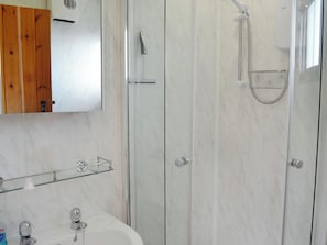 A bathroom with a marble wall, a wooden door, a glass shower enclosure, and a sink with a chrome faucet.