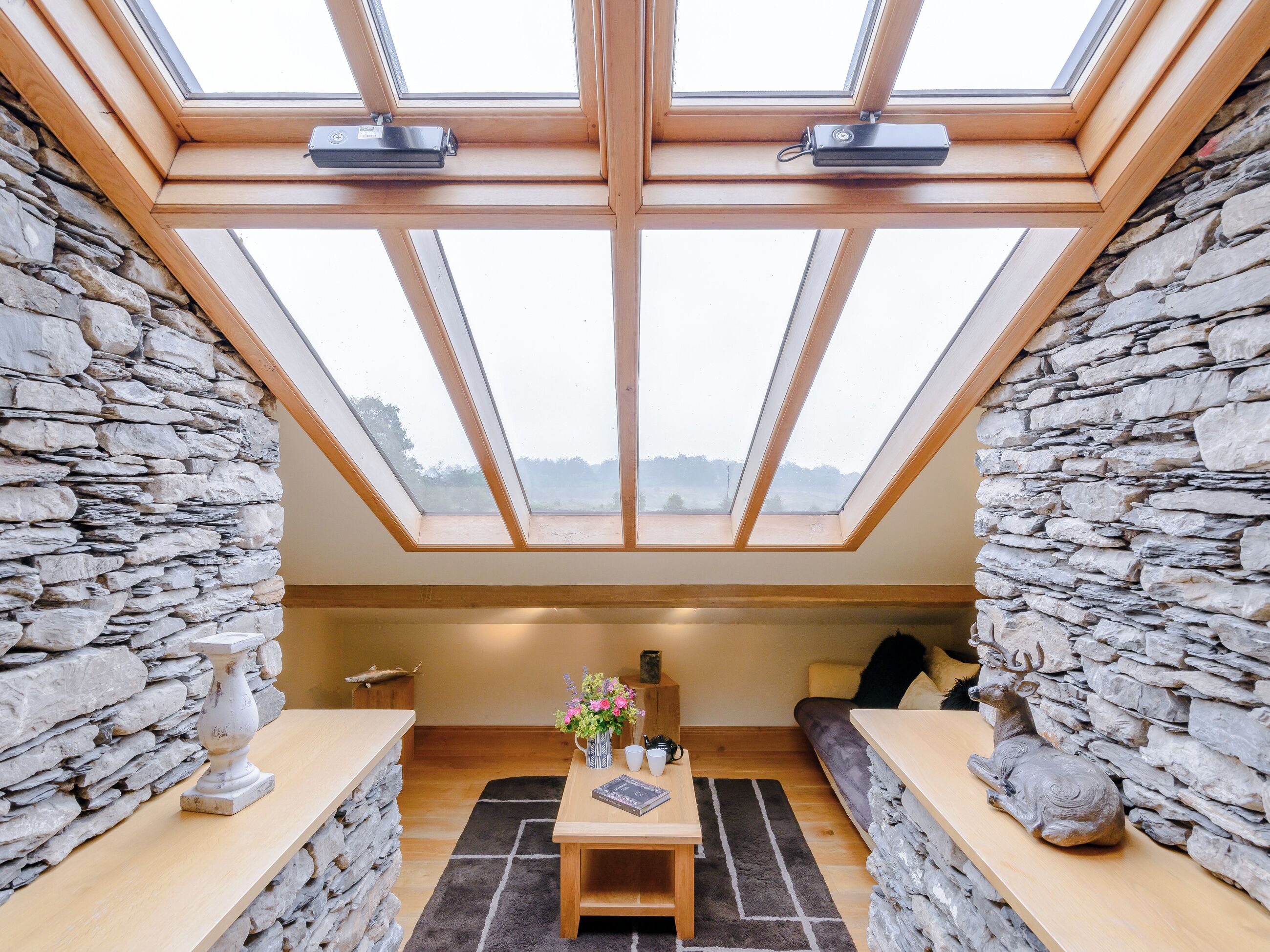 A room with a skylight, stone walls, a wooden table, and a sofa.