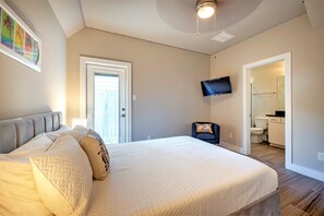 Une chambre à coucher avec un grand lit, un téléviseur fixé au mur et une porte donnant sur une salle de bain.