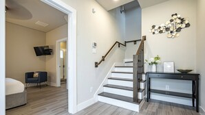 Ein modernes Wohnzimmer mit Treppe, einem an der Wand befestigten Flachbildfernseher und einem Beistelltisch mit Blumen.