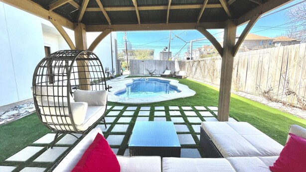 Ein Garten mit Swimmingpool, einer überdachten Terrasse mit Sitzgelegenheiten und einem Holzzaun.