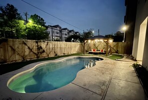 Un jardin avec une piscine, une clôture en bois et un espace salon abrité.