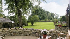 A stone wall, a wooden bench, a table with a potted plant, and a lawn in the background.