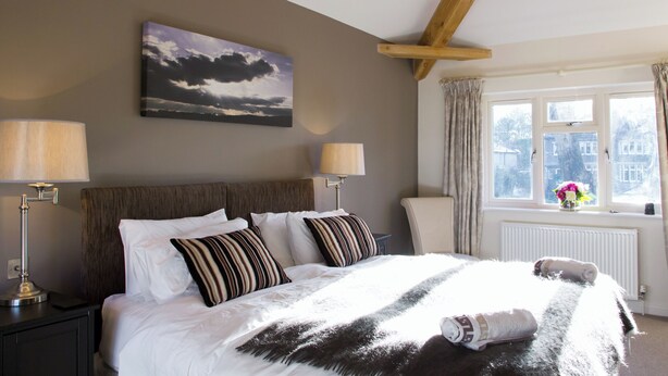 A bedroom with a bed, two bedside lamps, a chandelier, a window with curtains, and a painting on the wall.