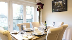 A dining table set for four with white chairs, a vase with flowers, and a wine bottle.