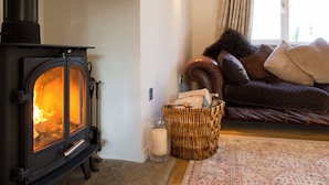 A cozy living room with a wood-burning stove, a comfortable sofa, a wicker basket, and a patterned rug.