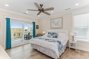 Une chambre avec un grand lit, un ventilateur de plafond, une fenêtre avec des stores et une vue sur l’extérieur.