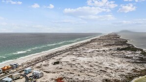 Ein Strand mit einer parallel zur Küste verlaufenden Straße, Gebäuden links und einem klaren Himmel.