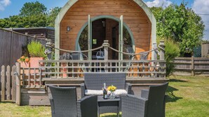 Une cabane en bois dotée d’une entrée en arc de cercle, d’un patio couvert avec des meubles en osier et d’une barrière faite de cordes.