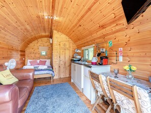 A cozy cabin with a wooden interior, a kitchenette, a dining area, and a bed with a blue rug.