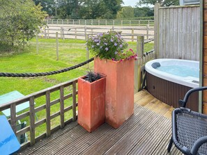 A wooden deck with a hot tub, two planters with flowers, and a rope barrier. - 1 bedroom accommodation in Northiam, near Rye (Northiam, near Rye)