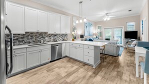 A modern kitchen with white cabinets, a large island, and a dining area with a TV.