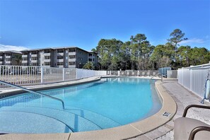 A swimming pool with a curved edge, surrounded by a white fence and a building with multiple balconies in the background. - 2 Blocks 2 Beach, Walk to Seaside, Pool, Beach Gear, New Kitchen (Santa Rosa Beach)