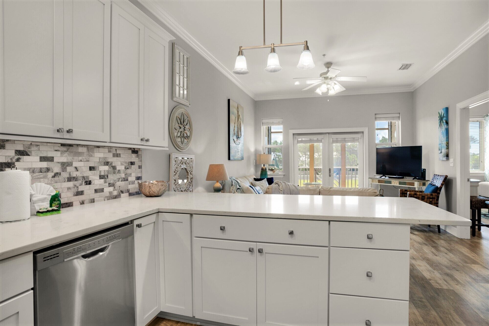 A modern kitchen with white cabinets, a dishwasher, a tiled backsplash, and a large island with a flat sink.