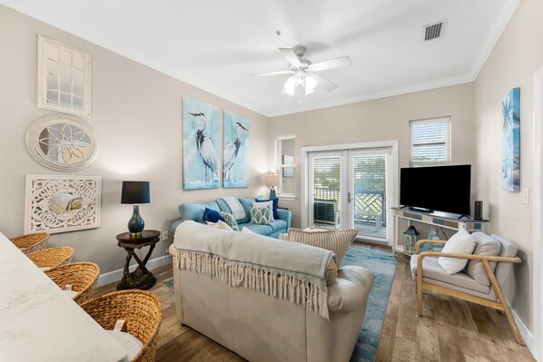 A living room with a beige sofa, a blue couch, wicker chairs, a TV, and artwork on the walls. - 2 Blocks 2 Beach, Walk to Seaside, Pool, Beach Gear, New Kitchen (Santa Rosa Beach)