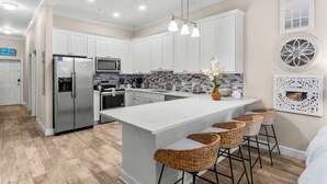 A modern kitchen with white cabinets, a large island with bar stools, stainless steel appliances, and decorative wall art.