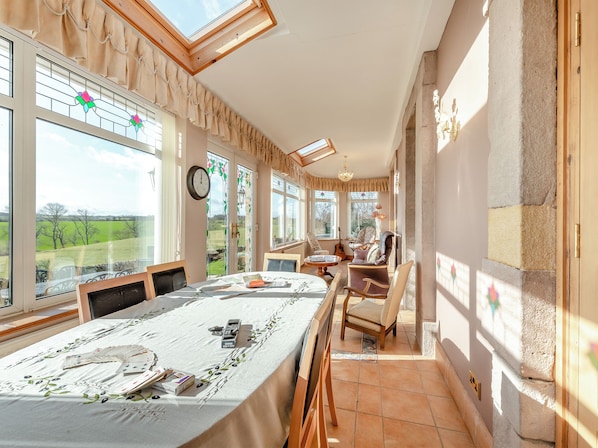 A dining area with a long table, chairs, and a view of the countryside through large windows.