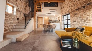 A spacious interior with stone walls, a wooden staircase, a dining area, and a yellow sofa. - Villa Terra Meera (Skradin)