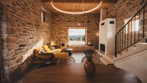 A rustic stone-walled room with a wooden ceiling, a round wooden table, a yellow sofa, and a staircase with a black railing. - Villa Terra Meera (Skradin)