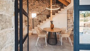 A stone-walled room with a round table and wicker chairs, a staircase with wooden railings, and a hanging light fixture. - Villa Terra Meera (Skradin)