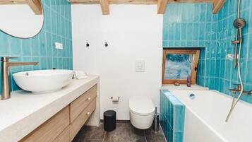 A bathroom with a large white sink, wooden cabinets, a white toilet, a bathtub with a showerhead, and a window with a view of trees.