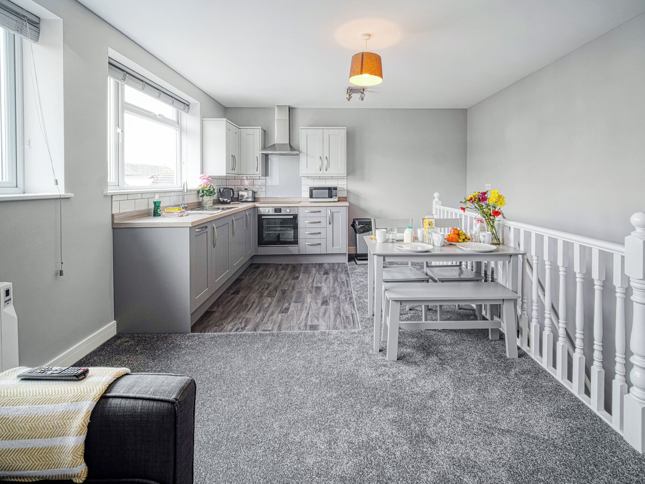 A modern kitchen with grey cabinets, a built-in oven, and a dining area with a table set for two.