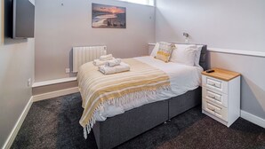 Un dormitorio moderno con una cama, una mesita de noche, un televisor, un radiador y una ventana con persianas.