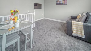 Una sala de estar moderna con comedor, alfombra gris, un sofá gris con una manta y un cuadro en la pared.