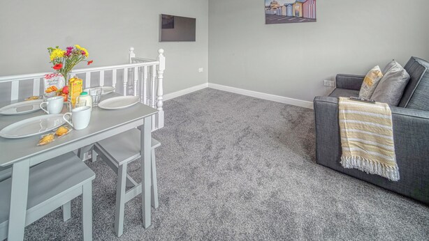 Una sala de estar moderna con comedor, alfombra gris, un sofá gris con una manta y un cuadro en la pared.