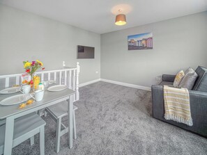 Een moderne woonkamer met een eethoek, grijs tapijt, een grijze bank met een plaid en een schilderij aan de muur.