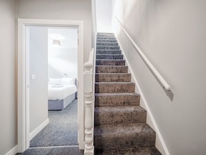 Eine Treppe mit Teppichstufen und einem weißen Geländer, die zu einem Schlafzimmer mit Bett und Nachttisch führt.