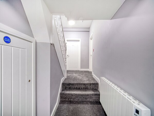 A narrow hallway with a carpeted staircase leading to a door.