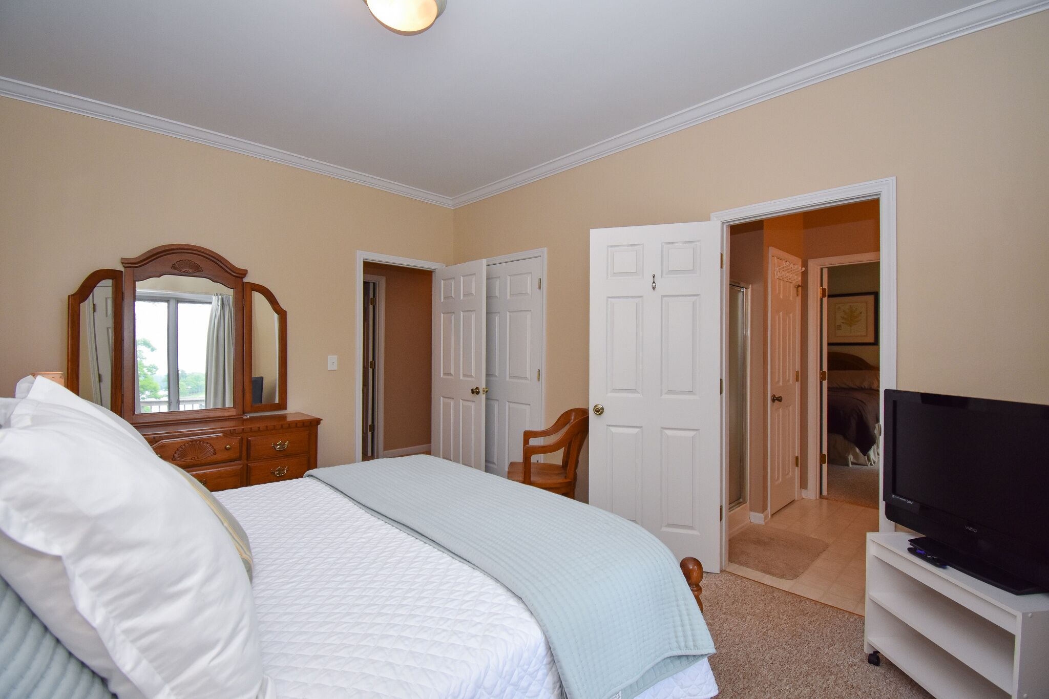 A bedroom with a bed, dresser, mirror, television, and a door leading to another room.