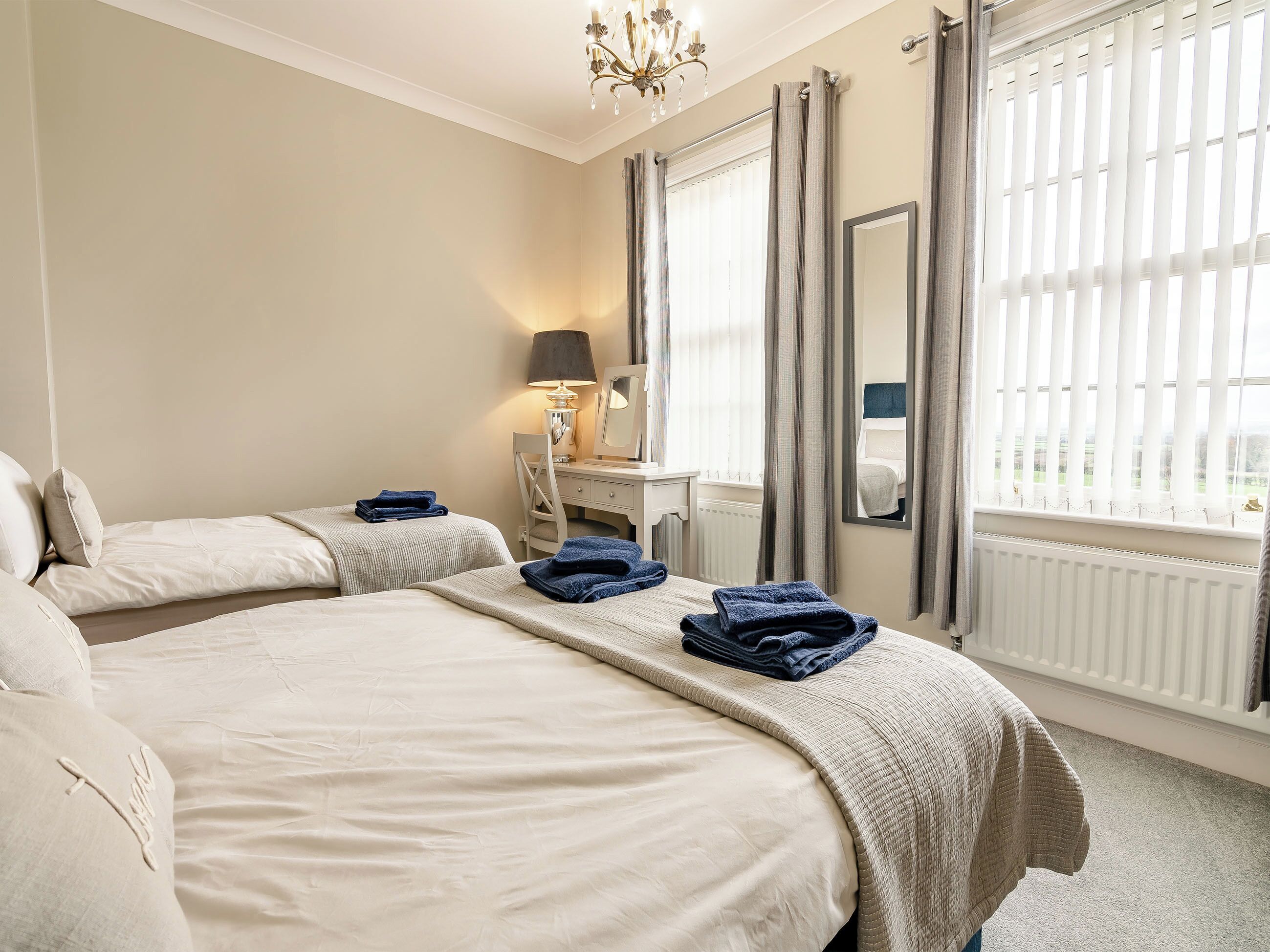 A hotel room with two beds, a desk, a chair, a lamp, and a window with curtains.