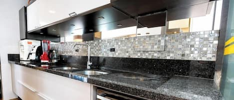 Una cocina moderna con encimera de granito negro, pileta de acero inoxidable y muebles de cocina blancos.