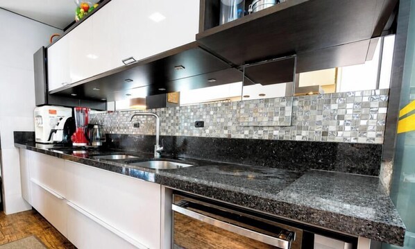A modern kitchen with a black granite countertop, stainless steel sink, and white cabinetry.