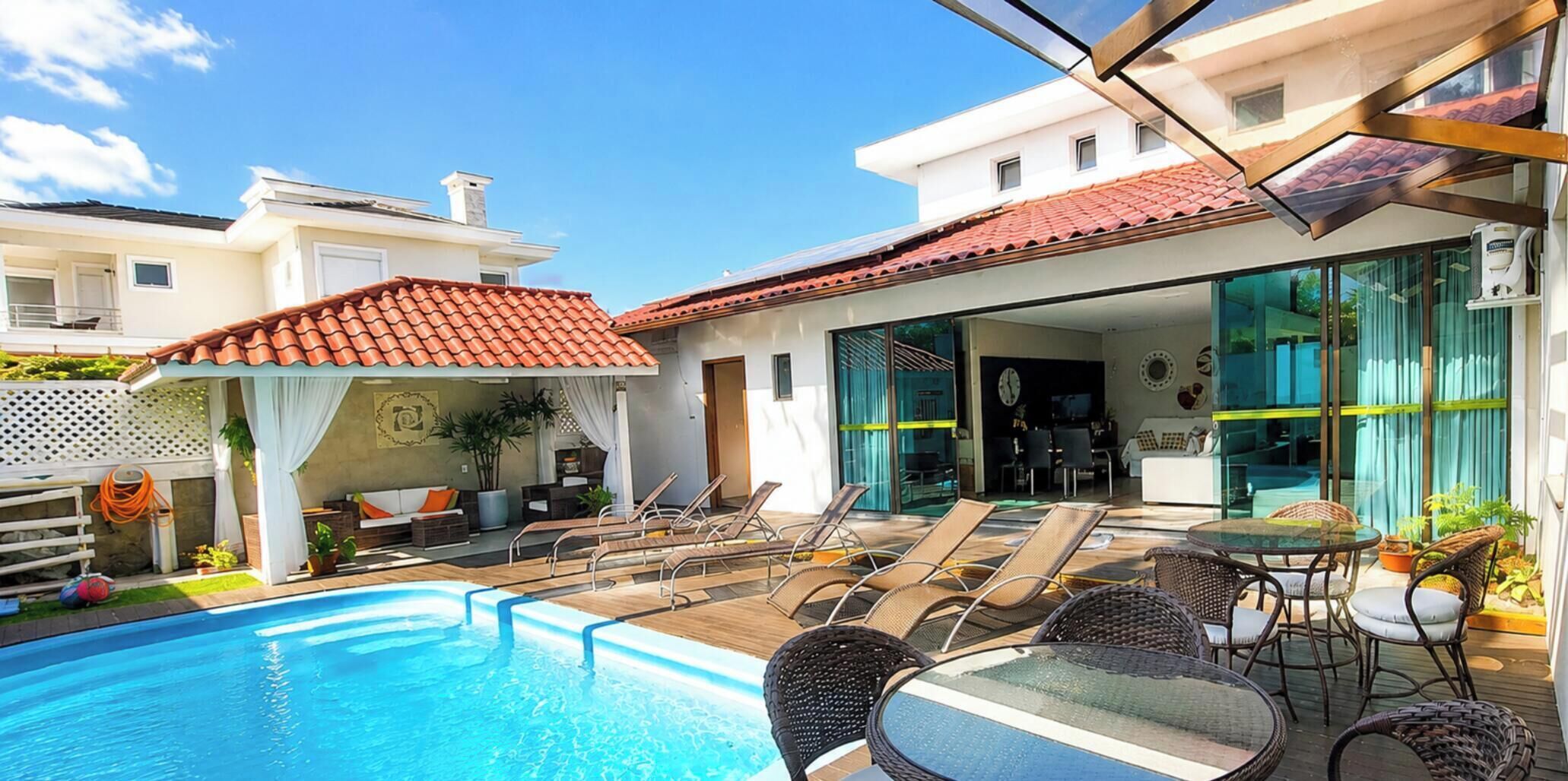 Piscina com espreguiçadeiras e área de refeições com parede de vidro.