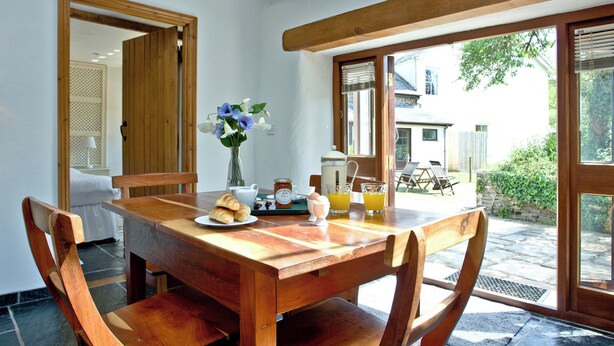 A wooden dining table with chairs, a vase with flowers, croissants, a pitcher, and glasses of orange juice. - 2 bedroom accommodation in Chulmleigh (Chulmleigh)