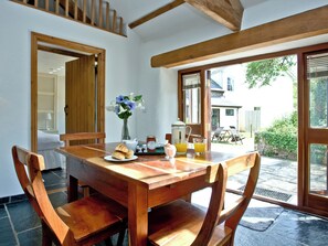 Una mesa de madera con sillas, un jarrón con flores, croissants, una jarra y vasos de zumo de naranja.