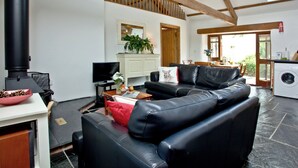 A modern living room with a black leather sofa, a television, and a fireplace. - 2 bedroom accommodation in Chulmleigh (Chulmleigh)