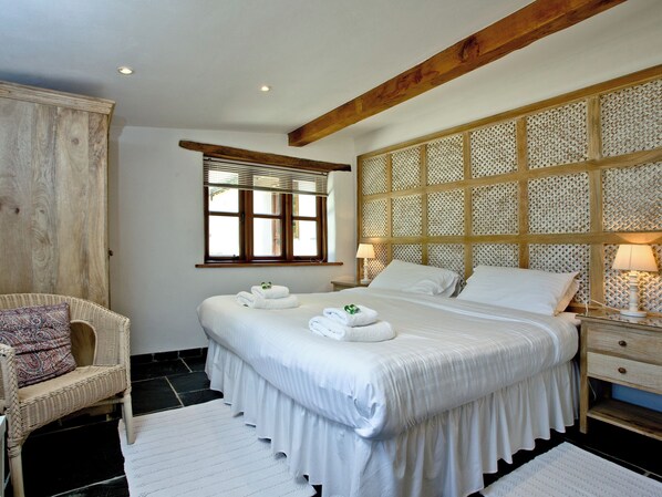 Un dormitorio con una cama grande, un cabecero de madera, una silla de mimbre y una ventana con persianas.