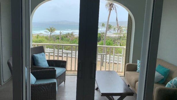 Un balcon doté de meubles en osier, d’une table et offrant une vue sur l’océan et la plage.