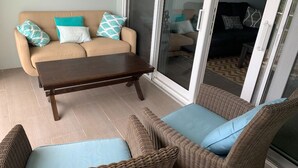 Un espace de vie comprenant un canapé beige, une table basse en bois et des chaises en osier avec des coussins bleus.