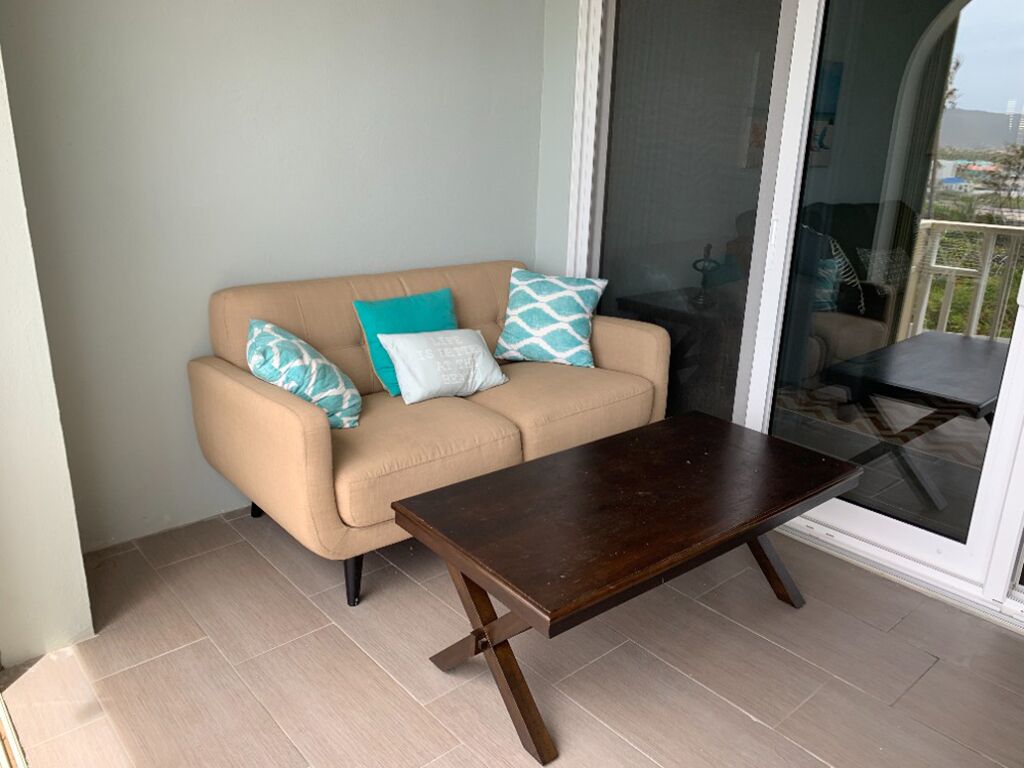 Un canapé beige agrémenté de coussins turquoise et blancs, une table basse en bois foncé et une porte-fenêtre coulissante donnant sur un espace extérieur.
