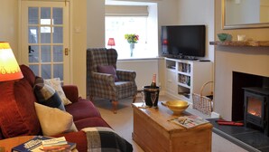 A living room with a sofa, armchair, television, fireplace, and a wooden coffee table. - Eden House Holiday Cottage (Pickering)