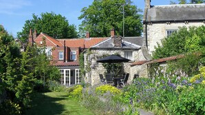 A stone house with a garden, a patio with chairs, and a clear sky. - Eden House Holiday Cottage (Pickering)